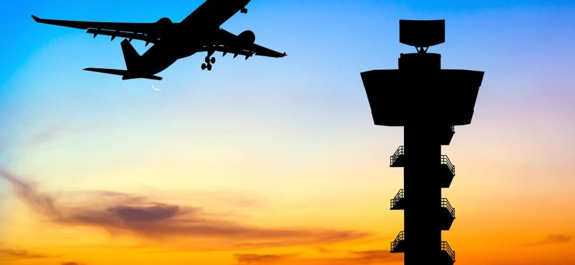 Silhouette commercial airplane take off over airport control tower at sunset