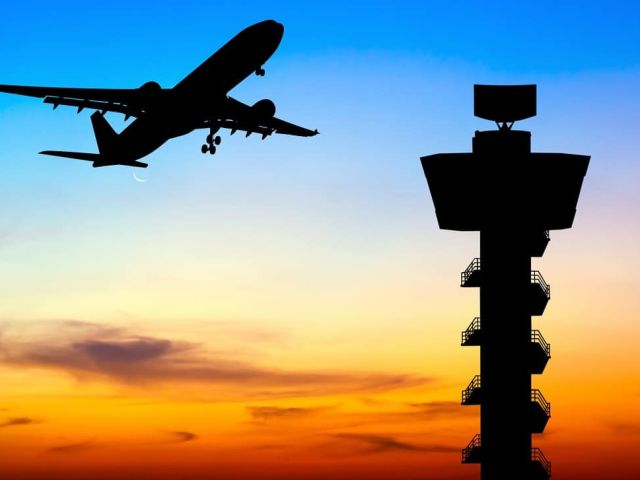 Silhouette commercial airplane take off over airport control tower at sunset