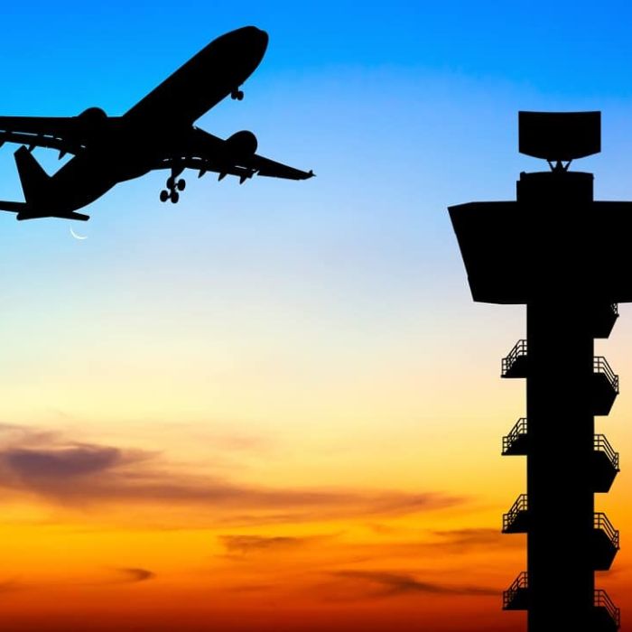 Silhouette commercial airplane take off over airport control tower at sunset